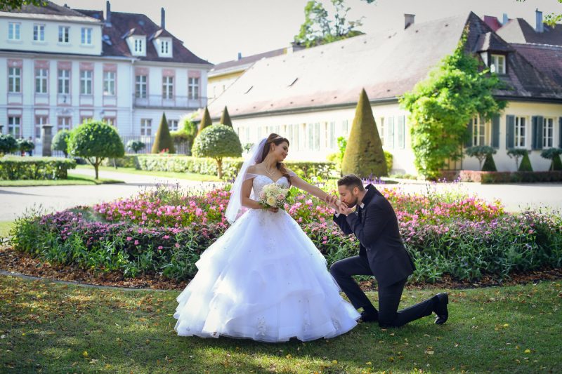 Bräutigam küsst die Hand der Braut vor der Orangerie in Ansbach